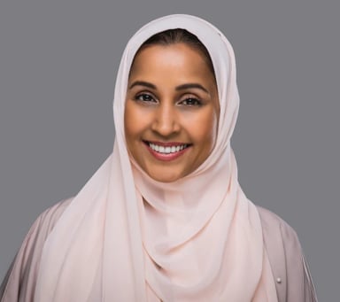Smiling woman in a light-colored hijab against a gray background