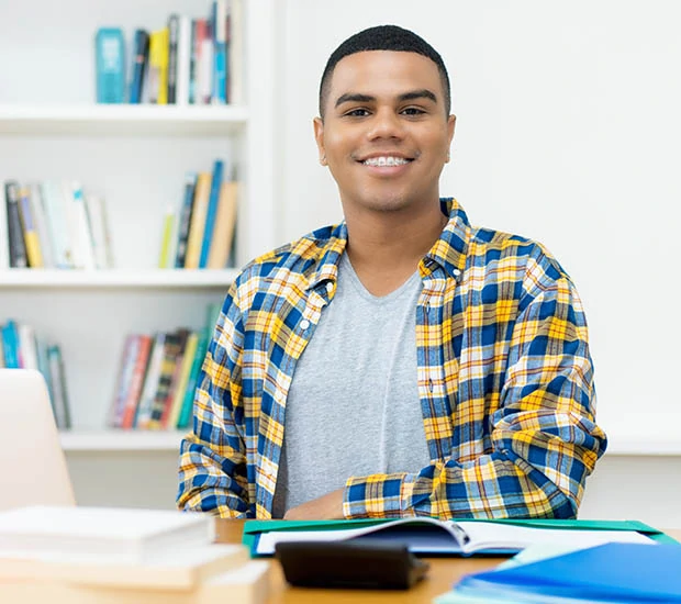 Smiling young man sitting at a desk with books and a laptop