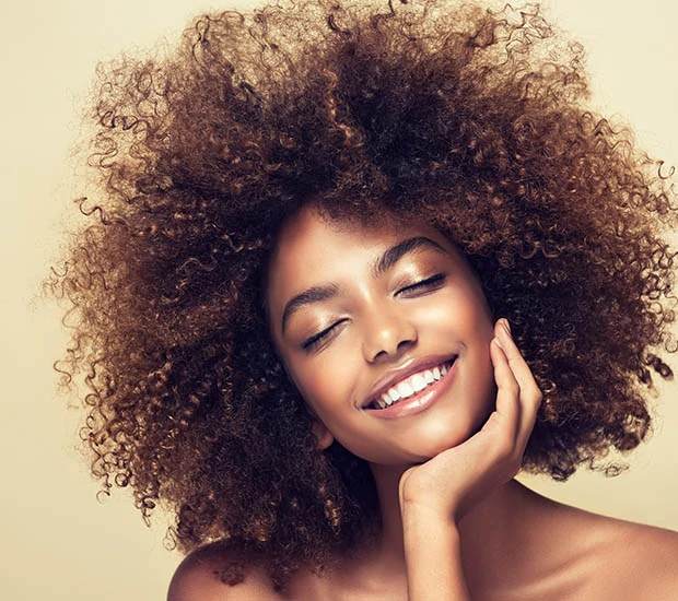 Woman with curly hair smiling warmly against a soft background